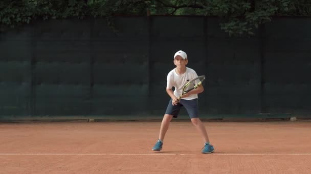 Амбітний тенісист хлопчик-підліток зосереджується і зосереджується на грі і ракетці ударний м'яч на червоному дворі — стокове відео