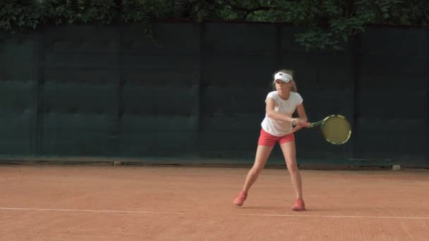 Rekabetçi ruh, azimli çocuk tenisçi kız konsantre oluyor ve kırmızı sahada raket topuna odaklanıyor. — Stok video
