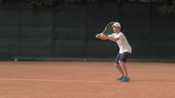 Играть в теннис, решительный спортсмен мальчик-подросток, концентрируясь и сосредоточившись на игре и ракетка бьет мяч на красной площадке — стоковое видео