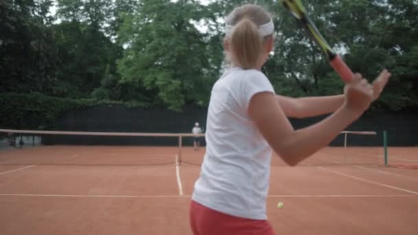 Професійний теніс, пара активних підлітків грають в теніс і м'яч кидають один одного через мережу на червоний корт під дощем — стокове відео