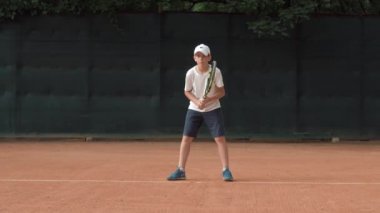 Tenis sportmenliği, hırslı çocuk konsantre olup oyuna odaklanıyor ve raket kırmızı sahada topu yeniyor.