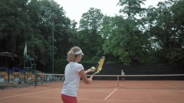 Tennis game, couple of sports children play tennis and ball throwing each other over net on red court on open air — ストック動画