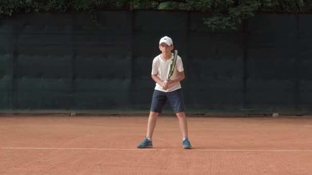 Tennis sportiviteit, ambitieuze kind jongen concentreren en zich richten op spel en racket beats bal op rode baan — Stockvideo