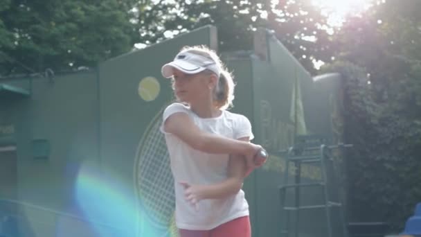 Purposeful and decisive teen girl tennis player with racket practising serve technique at training on court outdoors in bright sunlight — ストック動画