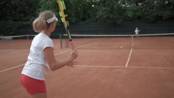 Тенісний матч, спортивний гравець дитяча дівчина з конкурсантом, який вдарив ракетку на м'яч, проходить через мережу один до одного в суді — стокове відео