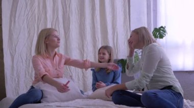 Aile sakin, anne ve kızlar yatakta otururken birbirlerine sarılıp sohbet ediyorlar.