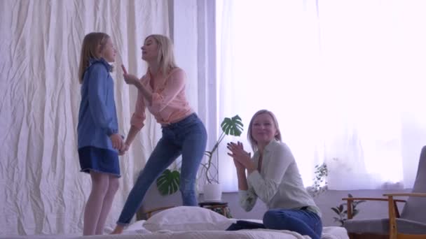 Щасливі вихідні вдома, сестри танцюють і співають для своєї мами, стоячи на ліжку — стокове відео