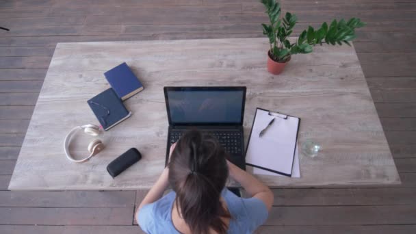 Student girl uses laptop while typing text on keyboard and writes notes in clipboard sitting at desk during e-learning, top view — ストック動画