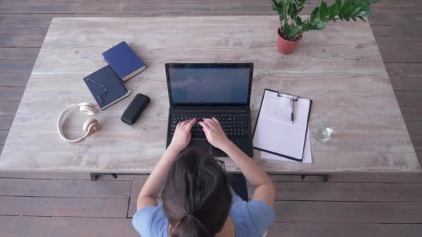 Giorno lavorativo, vista dall'alto della giovane donna che digita testo sulla tastiera del computer portatile e scrive appunti negli appunti seduti alla scrivania — Video Stock