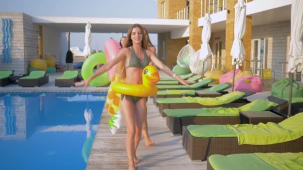 Šťastný atraktivní přítelkyně do plavek s nafukovacími kroužky chodit v blízkosti bazénu během letní dovolené v letovisku — Stock video