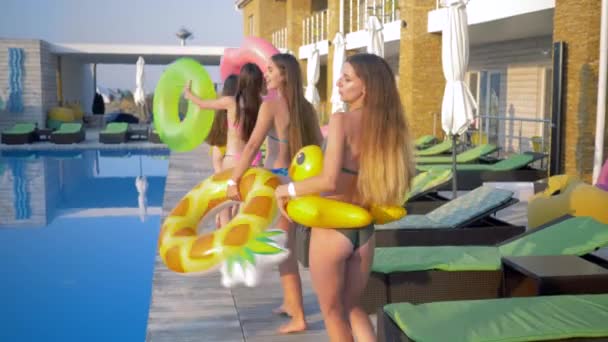 Amigos felices chicas en traje de baño con anillos inflables que se divierten cerca de la piscina durante las vacaciones de verano en el complejo — Vídeos de Stock