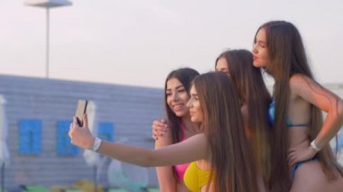 Yaz tatili, uzun saçlı mayo giyen kızlar tatil köyünde dinlenirken cep telefonlarında selfie çekiyorlar.