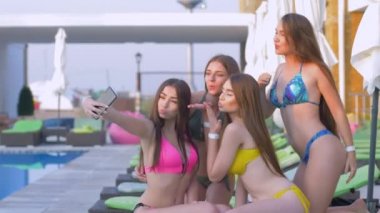 Yaz haftasonu, uzun saçlı, mayo giyen mutlu bir kadın tatil köyünde yüzme havuzunun yanında dinlenirken akıllı telefondan selfie çekiyor.