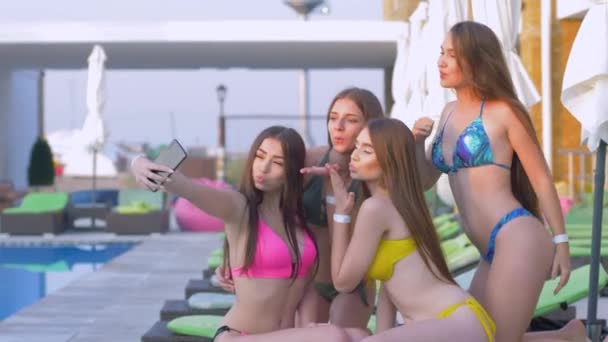 Літні вихідні, компанія щаслива жінка з довгим волоссям у купальнику фотографує селфі на смартфоні, відпочиваючи біля басейну на курорті — стокове відео