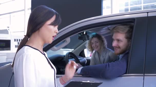 Auto business, verkoopster adviseren klanten jong stel zitten in de auto salon, terwijl het kopen van familie voertuig op de autoshow — Stockvideo