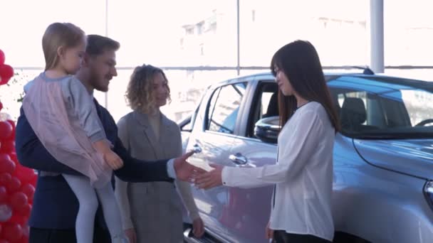 Auto negocio, familia feliz joven con hija compra automóvil y la vendedora asiática da las llaves de las manos en el centro de ventas de automóviles — Vídeos de Stock