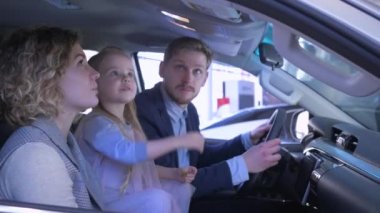 Araba galerisi, neşeli anne ve baba ve çocuk arabası aile otomobili incelemesi ve kabinde otururken pozitif parmak hareketi.