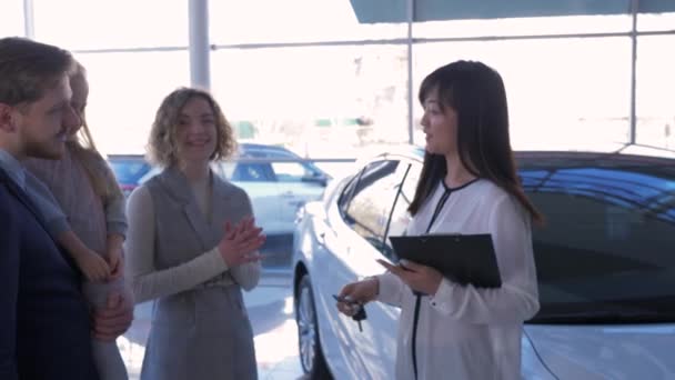 Auto kopen, jonge vrolijke familie met kind koopt machine en manager Aziatische vrouw geeft handen sleutels bij auto salon — Stockvideo