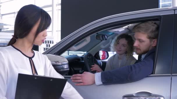 Auto verkoper aziatische vrouw raadplegen consumenten jong gezin zitten in auto salon terwijl het kopen van auto bij showroom — Stockvideo