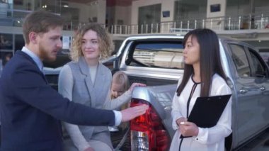 Aile otomobil satın alma, araba satıcısı müşteriler için araç seçmeye yardım ediyor. Çocuk sahibi genç çift araba satış merkezindeki yeni makinenin bagajında.