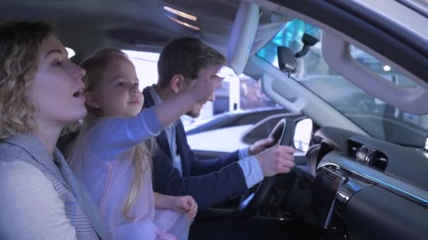 Family in auto show, lucky parents with child girl chooses vehicle and give thumbs up while sitting in cabin at car sale center — Stock Video