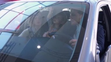 Mutlu aile yeni bir araba alır, kızıyla birlikte gülümseyen kadın ve erkek otomobili incelerken araba galerisinde oturur, ön camdan bakar.
