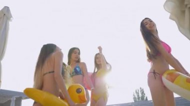 Pahalı bir tatil köyünde havuz kenarında mayo giyip eğlenen çekici kızlarla dolu neşeli bir şirket.