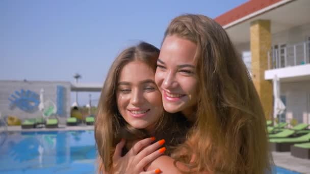 Portrait de petites amies heureuses, étreinte émotionnelle de belles meilleures amies près de la piscine bleue pendant les vacances d'été dans une station balnéaire chère — Video