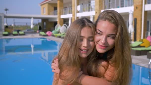 Portrait de filles heureuses amis, mignonne jeune femme aux cheveux longs et belle peau se serrant joyeusement dans leurs bras posant pour appareil photo dans une station riche pendant les vacances d'été — Video