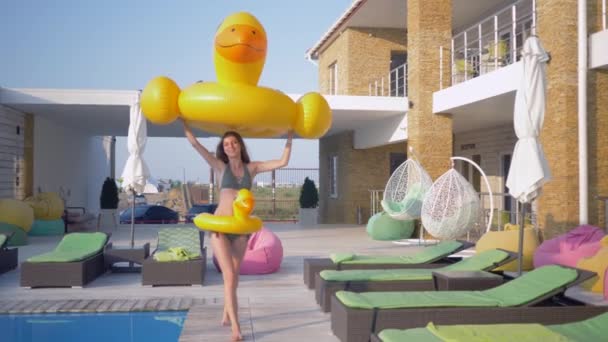 Zomervakantie, gelukkig mooi jong meisje met perfect lichaam en lang haar in de buurt van het zwembad spelen met opblaasbare ringen tijdens vakantie in luxe resort — Stockvideo