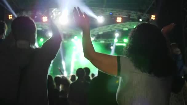 Aktivní mladík s rukama nad hlavou tleskání a skok před jasně osvětleným jevištěm na festivalu v noci — Stock video
