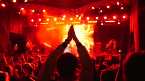 Multidão de pessoas batendo palmas sobre cabeças no festival de rock iluminado por holofotes brilhantes — Vídeo de Stock