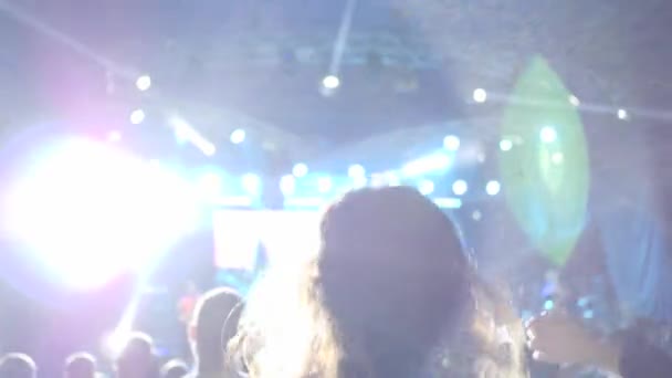 Multitud extática saltando con los brazos arriba disfrutando de música en vivo antes de escenario brillantemente iluminado en el festival en la noche — Vídeo de stock