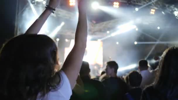 Ventiladores extáticos con las manos levantadas saltando antes de escenario brillantemente iluminado en concierto de rock — Vídeo de stock