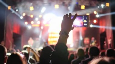 Parlak sahne ışıklarıyla arka plandaki rock konserinde fan kayıtlarının videolarına akıllı telefon bağlandı
