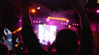 Arka planda elleri havada, sahne ışıkları altında konser veren bir kalabalık.