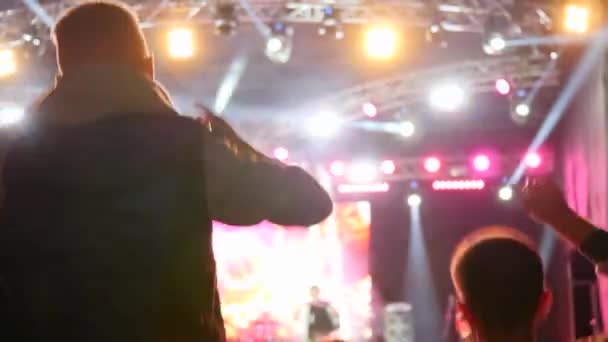 Přátelé se zvednutými pažemi skákání s potěšením na koncertu na pozadí jeviště osvětlené světlomety — Stock video