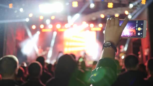 Πρόσωπο καταγράφει βίντεο στο κινητό τηλέφωνο στο πλήθος φόντο σε φωτεινά φώτα σε ροκ συναυλία — Αρχείο Βίντεο
