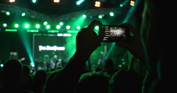 Sylwetka osoby nagrywa wideo na telefon komórkowy na tle tłumu na koncercie w jasnych światłach — Wideo stockowe