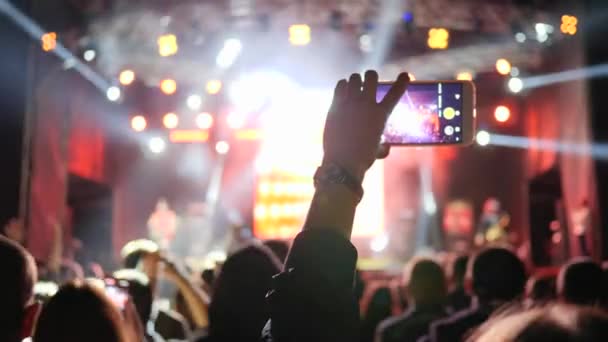 Smartphone in handen van fan records video op rockconcert op achtergrond menigte in helder podium lichten — Stockvideo