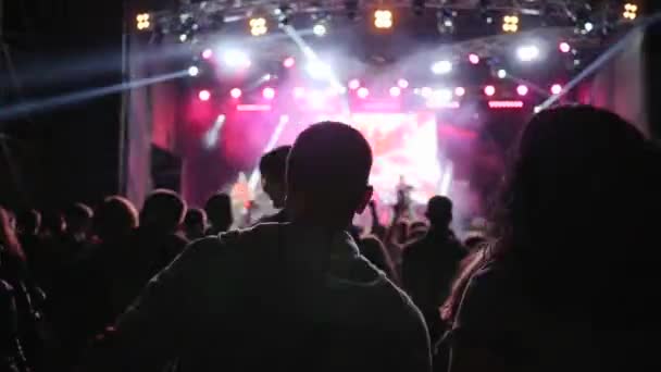 Bailando juventud con los brazos levantados divirtiéndose en el fondo del escenario brillantemente iluminado en el evento nocturno — Vídeo de stock