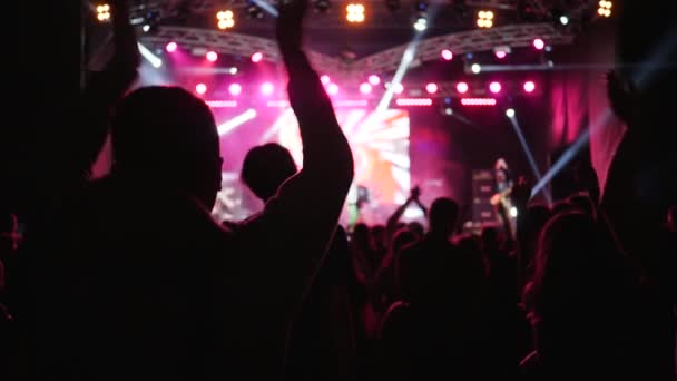 Active people clapping with arms raised and jumping on background of brightly lit stage at rock festival — Stockvideo