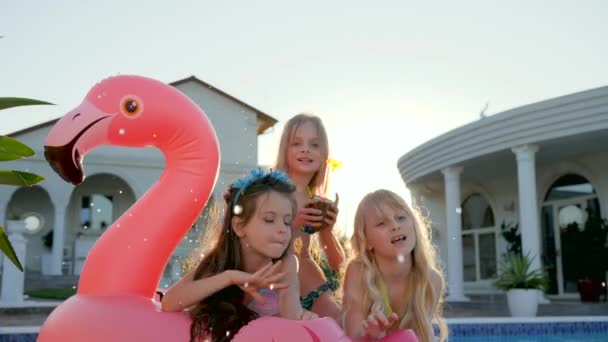 夏休みに水着を着た子供たちの有名人女の子はプールの近くの膨脹可能なピンクフラミンゴに横たわっています — ストック動画