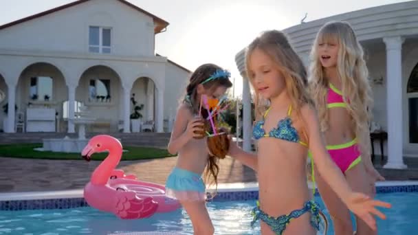 Niñas agradables cerca de la villa con cócteles tropicales al aire libre, niños ricos discuten secretos femeninos en la piscina de fondo — Vídeo de stock