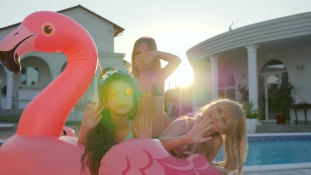Small girlfriends on summer vacation, sweet girls lie on inflatable pink flamingo near pool, spoiled rich childs in backlight — Stock Video