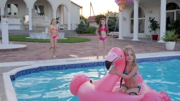 Niña en traje de baño saltando a la piscina de verano, niño bonito en flamenco inflable nadar en la piscina, salto alegre — Vídeos de Stock