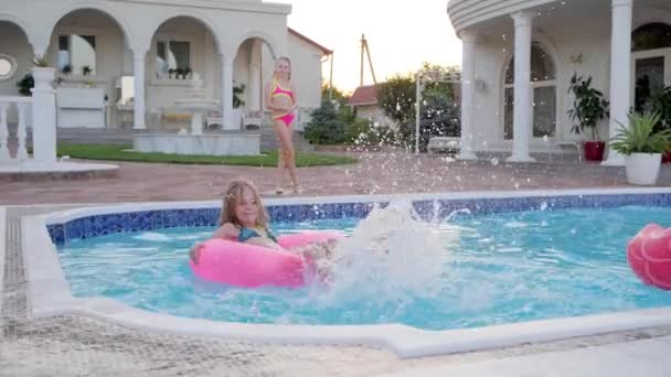 Niña nadando en el anillo inflable y da salpicaduras de agua en la piscina, las hermanas pequeñas ricas pasan el verano — Vídeos de Stock