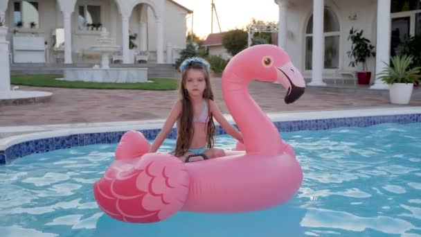 Criança triste de pais ricos Férias de verão na mansão, menina em roupa de banho nadando no flamingo rosa inflável na piscina, fim de semana rico — Vídeo de Stock