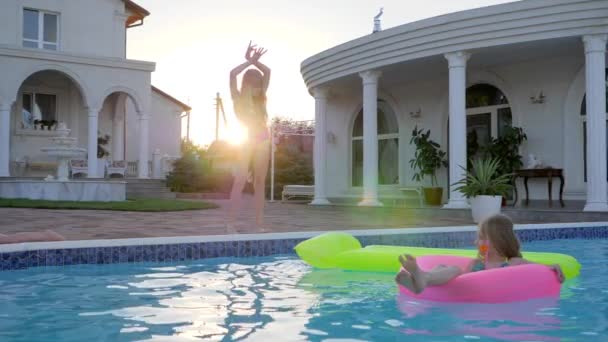 Süßes Kind im aufblasbaren Ring schwimmt im Pool im Sonnenlicht, kleines Mädchen im Badeanzug tanzt am Pool, — Stockvideo