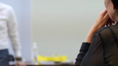 Kadın yüzünün yanında el ele tutuşup konferans salonundaki konuşmacıyı dikkatle dinliyor.